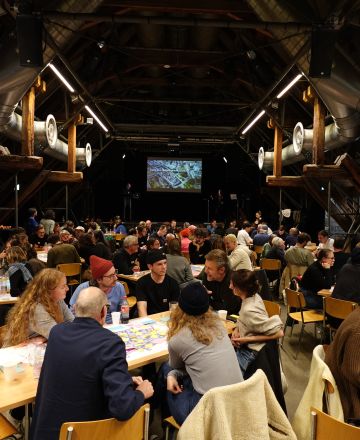 Im grossen Saal in der Schüür gab es drei Tischreihen, an denen verschiedene Leute sitzen. viele 