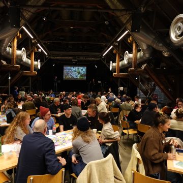 Im grossen Saal in der Schüür gab es drei Tischreihen, an denen verschiedene Leute sitzen. viele 