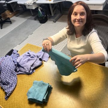 Ich sitze am Tisch, lächle in die Kamera und halte einen grünen Lappen in der Hand.