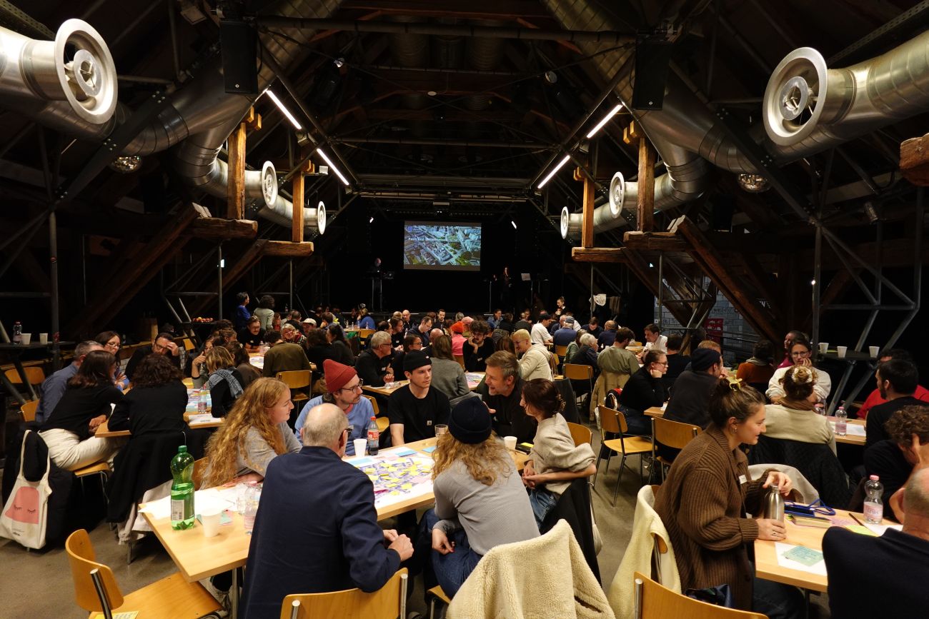 Im grossen Saal in der Schüür gab es drei Tischreihen, an denen verschiedene Leute sitzen. viele 