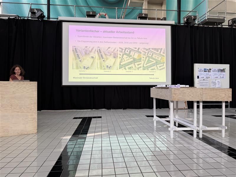 Auf der Leinwand sieht man den aktuellen Stand der Planung, davor ein Podest, wo Carmen Baumann den Ablauf erklärt.