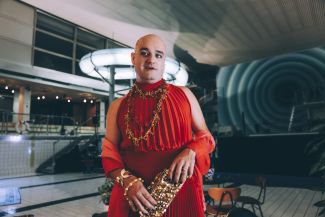 Eine in rot angekleidete Person mit einer goldenen Handtasche im Neubad Pool, im Hintergrund leuchtet die Rutschbahn bläulich.