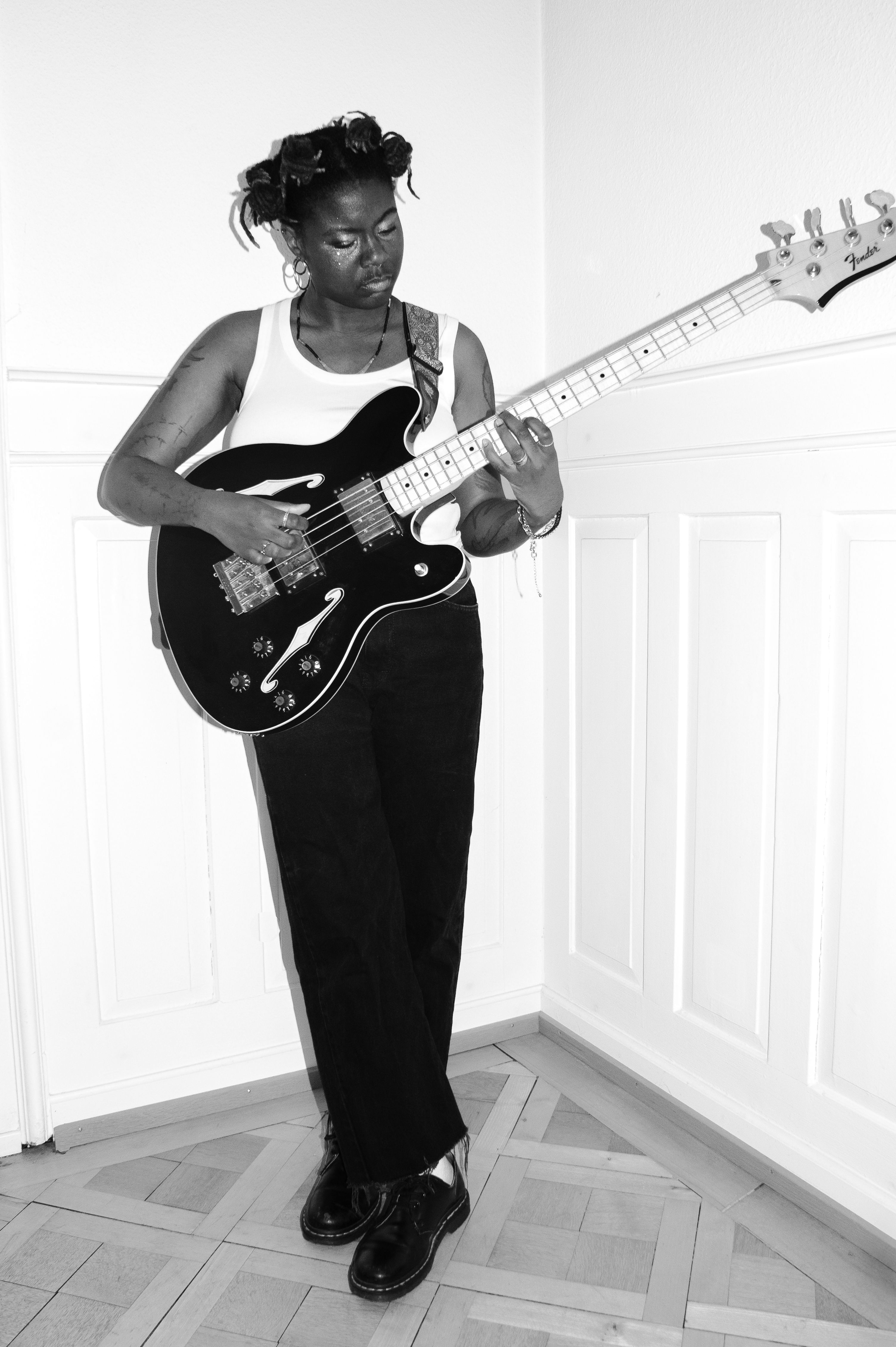 Künstlerperson mit Bassgitarre vor schwarz-weissem Hintergrund (Schwarzweissfotografie)