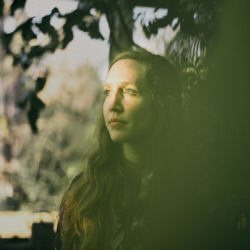Frau mit langen Haaren und im Hintergrund Blätter