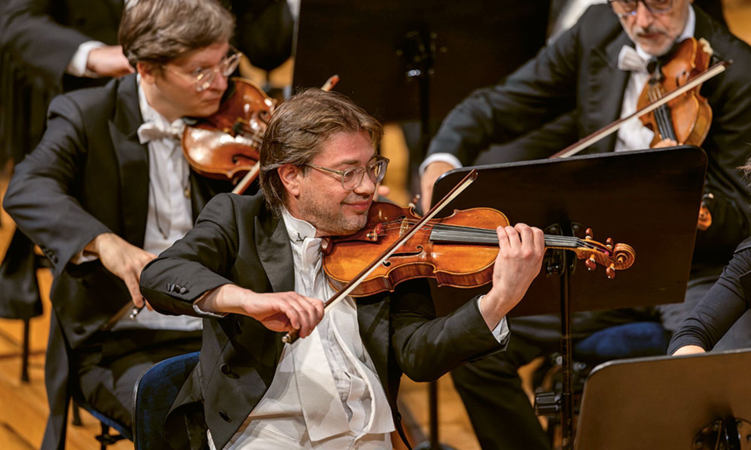 Auf dem Bild sind drei Personen zu sehen, die Violine spielen
