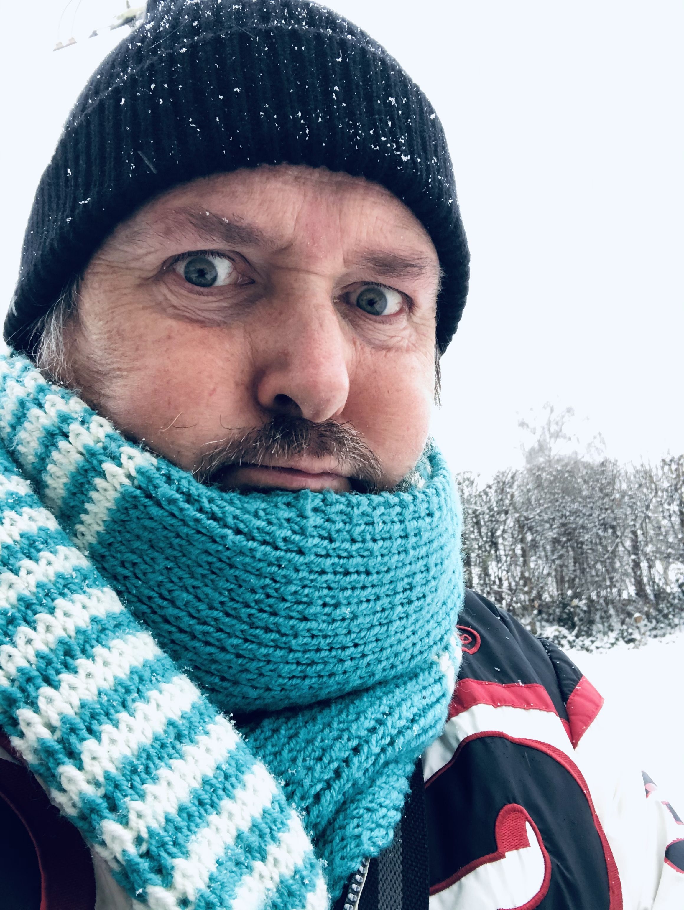 Matto Kämpf mit türkis-weiss-gestreiftem Schal und einer dunklen Wollmütze auf dem Kopf. Im Hintergrund ein Wald in einer Schneelandschaft